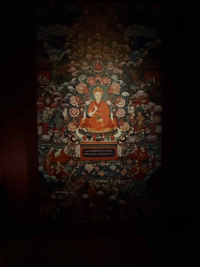 燈光下呈現的乾隆皇帝唐卡形象，佔據蓮座中央，周圍以繁複佛教圖像與護法環繞，展現十八世紀清宮以唐卡視覺語法建構皇帝神性與權威的策略；拍攝於香港故宮文化博物館。