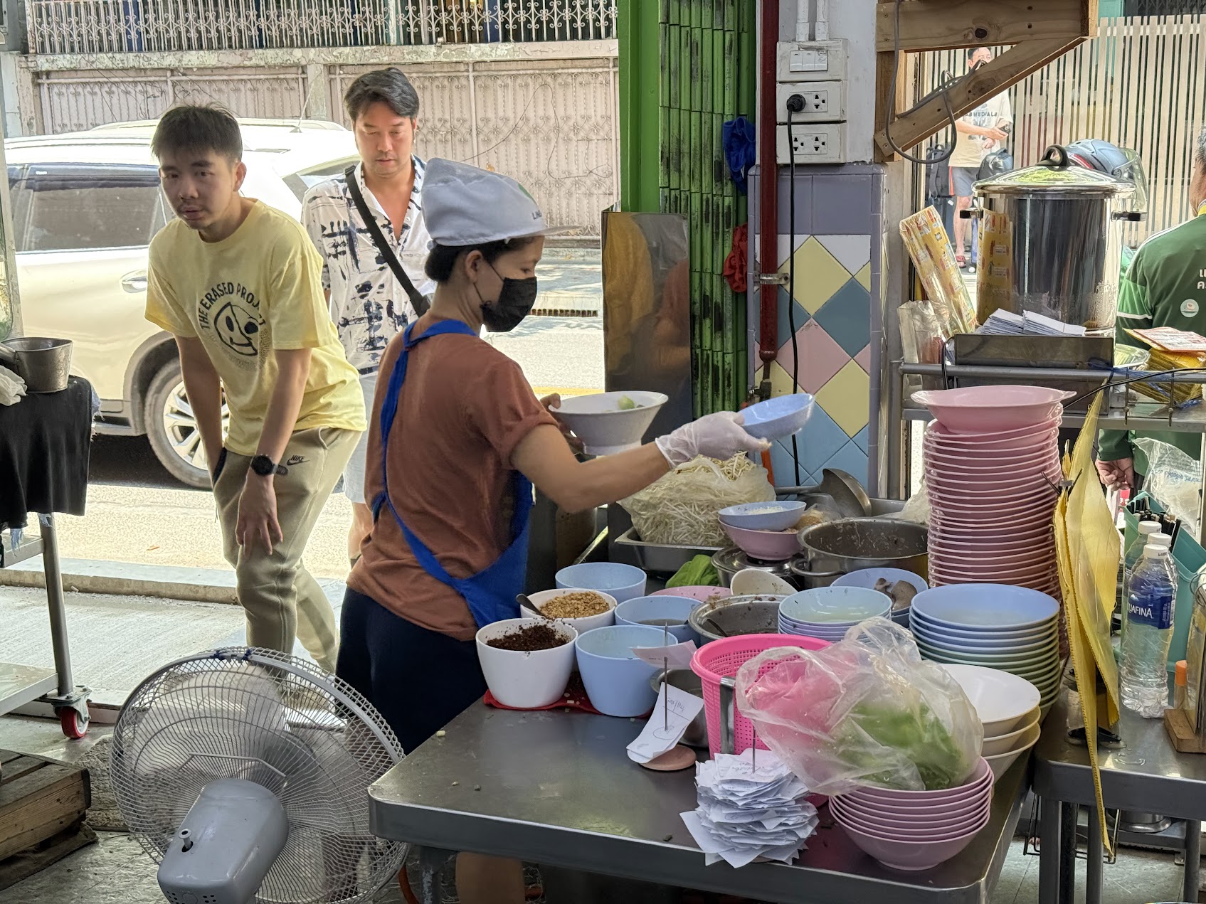 バンコクの麺店の仕込み台で、手際よく丼を組み立てていく様子。港市につながる都市のスープ文化と労働のリズムが見える