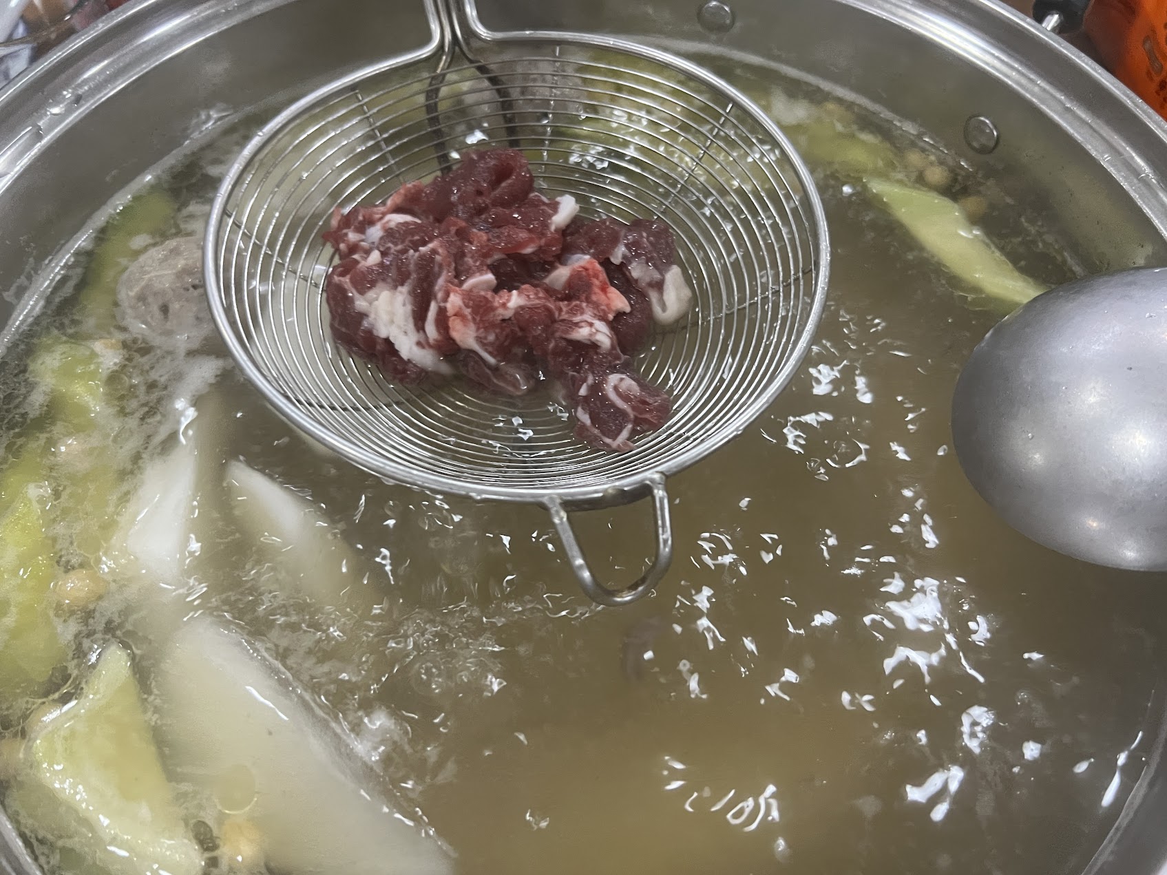 網じゃくしで新鮮な牛肉を澄んだ湯にさっと通している場面。潮汕の鮮牛肉火鍋に見られる技術的な動きを示している。