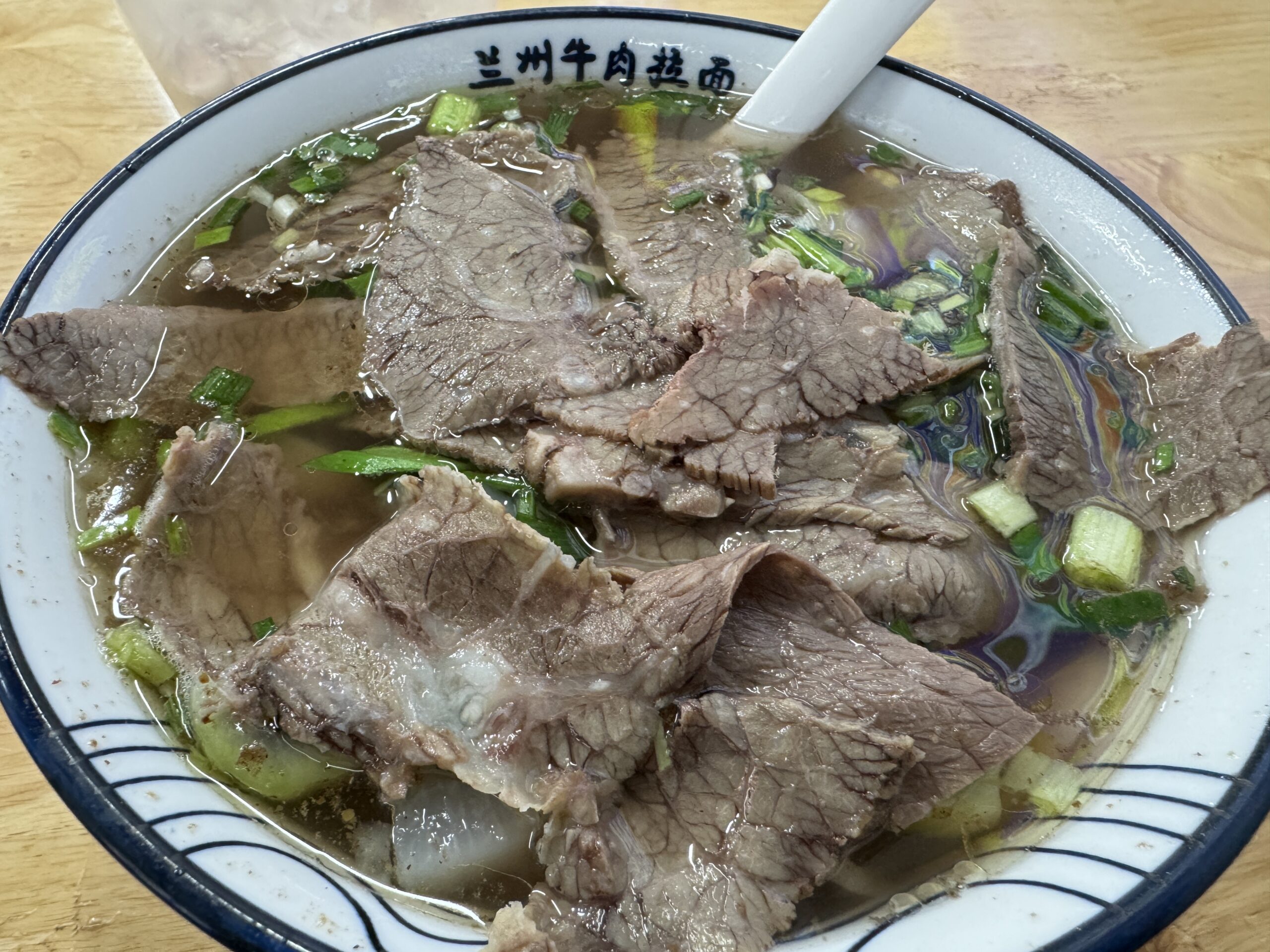 牛肉が何枚も載り、ねぎと澄んだ牛骨スープが見える蘭州風の清湯牛肉麺。