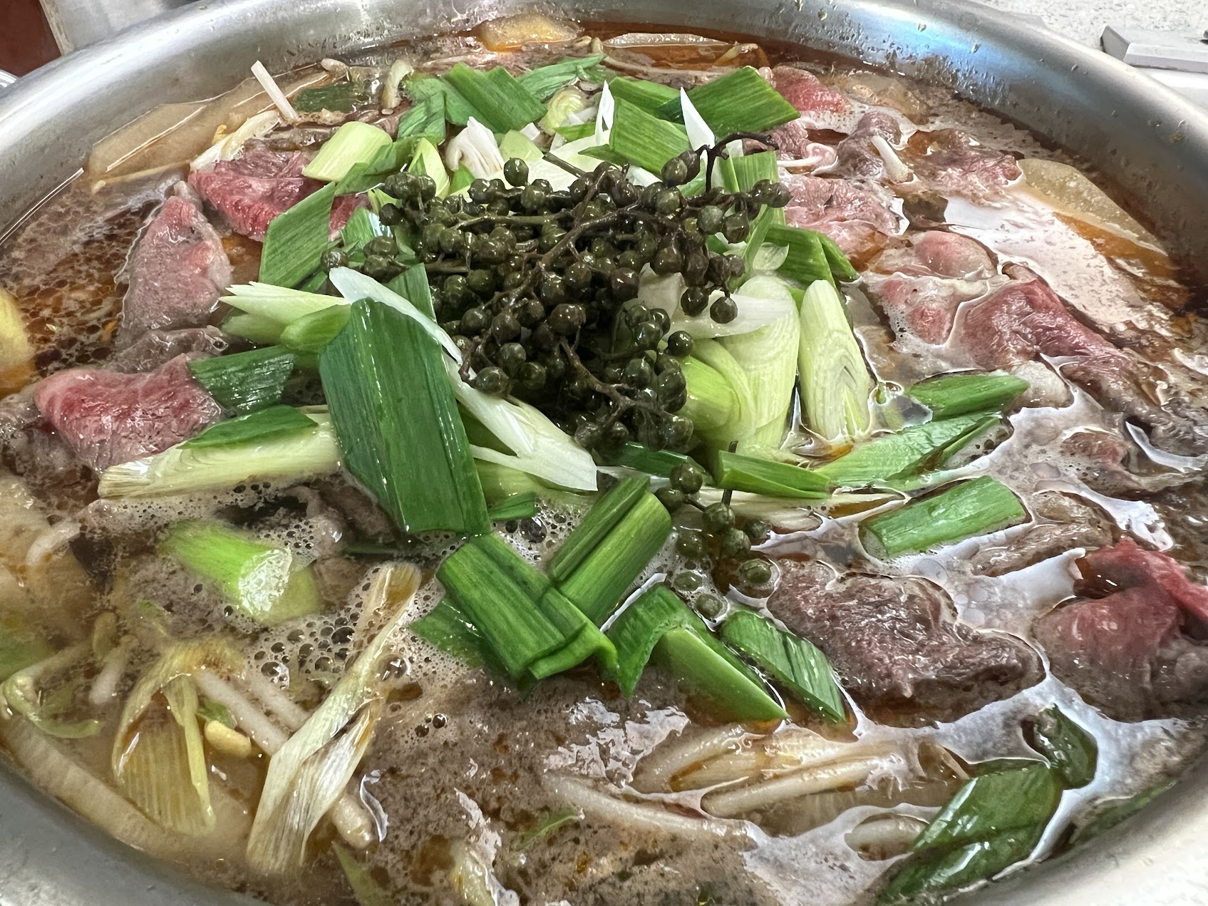 鍋の中で煮込まれる牛肉のスープ。牛肉の塊、青ねぎ、香味素材が見える。