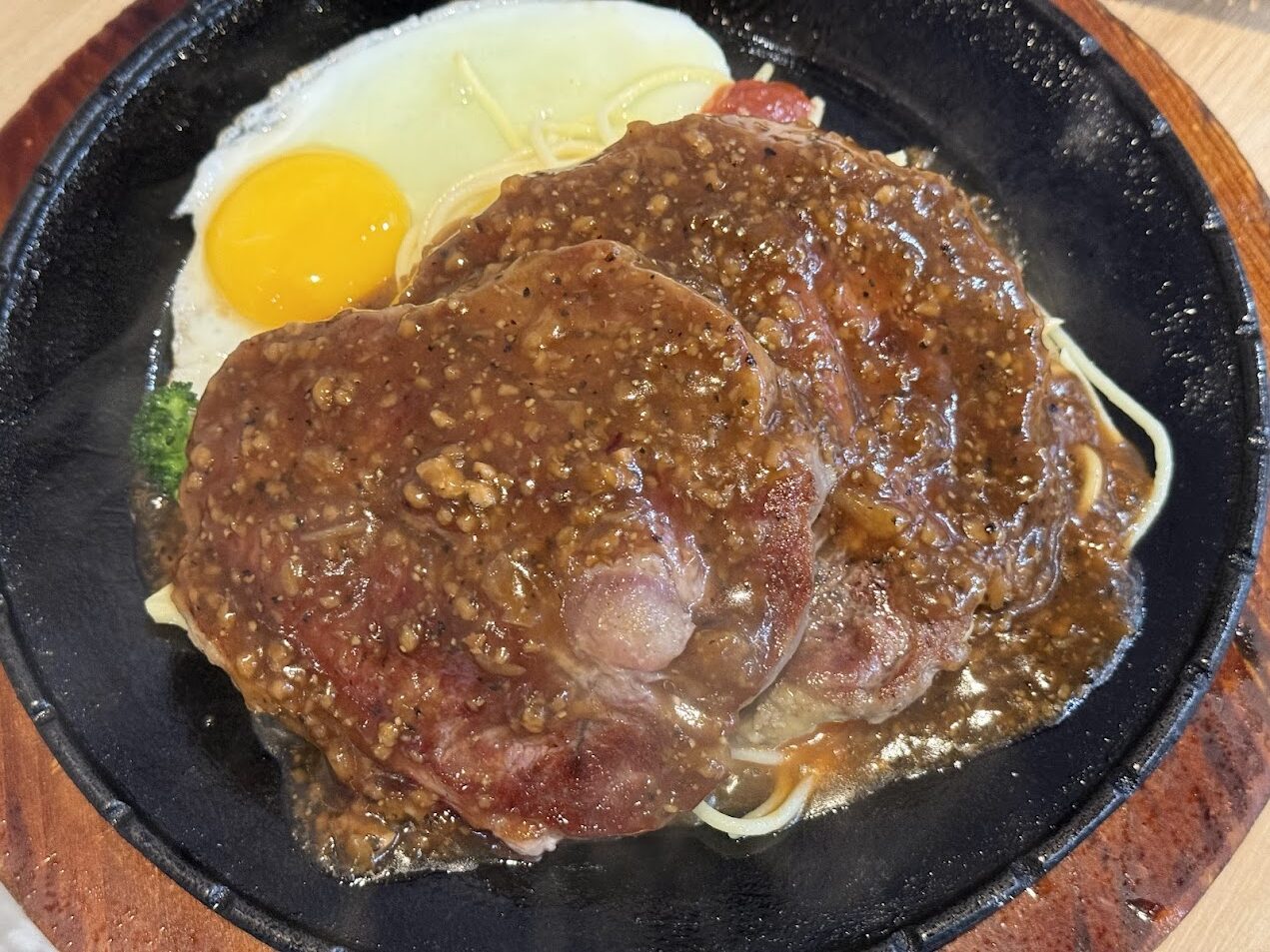 一份台灣夜市風格的鐵板牛排，搭配麵條、煎蛋與濃厚黑胡椒醬，呈現在熱鐵板上