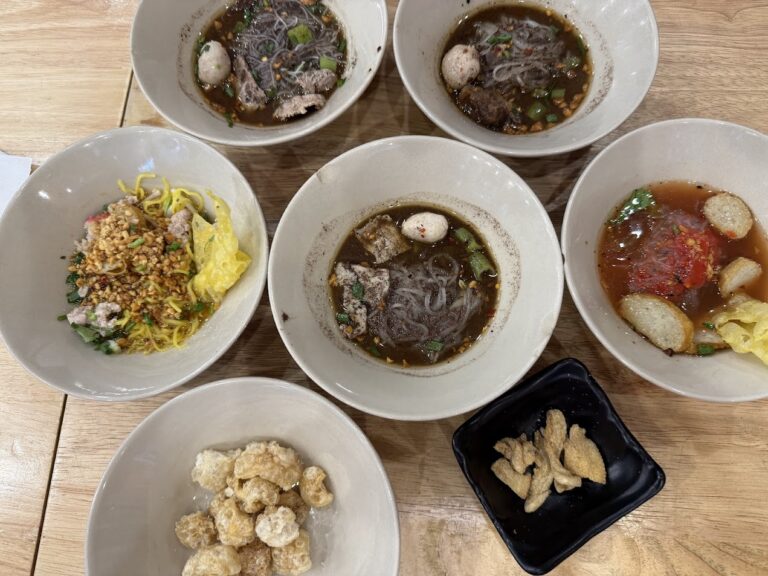 桌上擺著多碗不同版本的泰式船麵與配菜，有深色湯頭、乾拌、丸子與炸物配料
