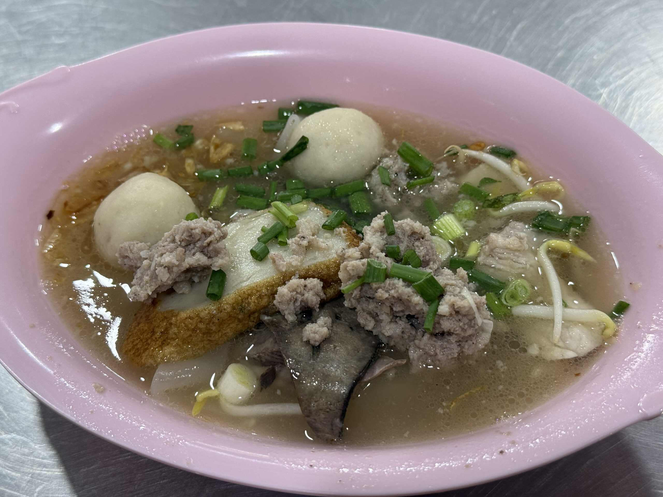 粉紅色碗中的泰式豬肉清湯麵，配有魚丸、絞肉、豆芽、豬肝與蔥花，呈現街邊豬肉粉常見組合