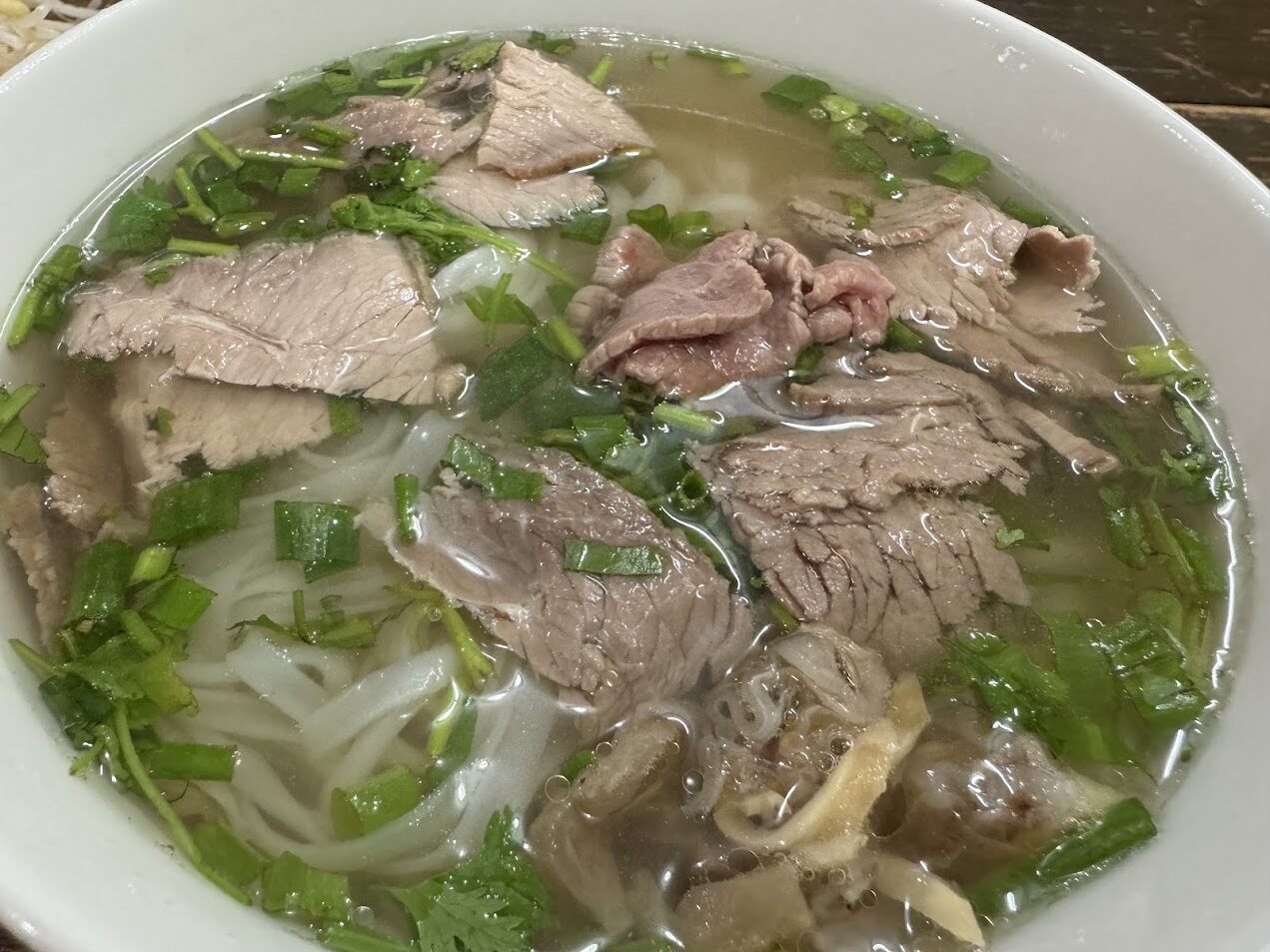 薄切り牛肉、澄んだスープ、米麺、青ねぎ、香草が見えるベトナムのフォー。鮮牛肉の清湯系システムの典型的な構造を示している。