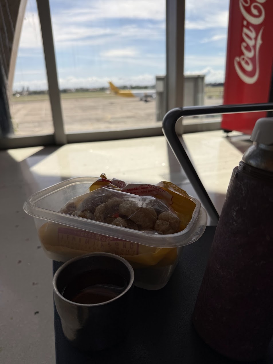 空港の待合空間に置かれた chicharon と自分で淹れた茶。豚皮揚げが単なる零食ではなく、移動の途中で身体を支える簡易な補給食にもなりうることを示している。