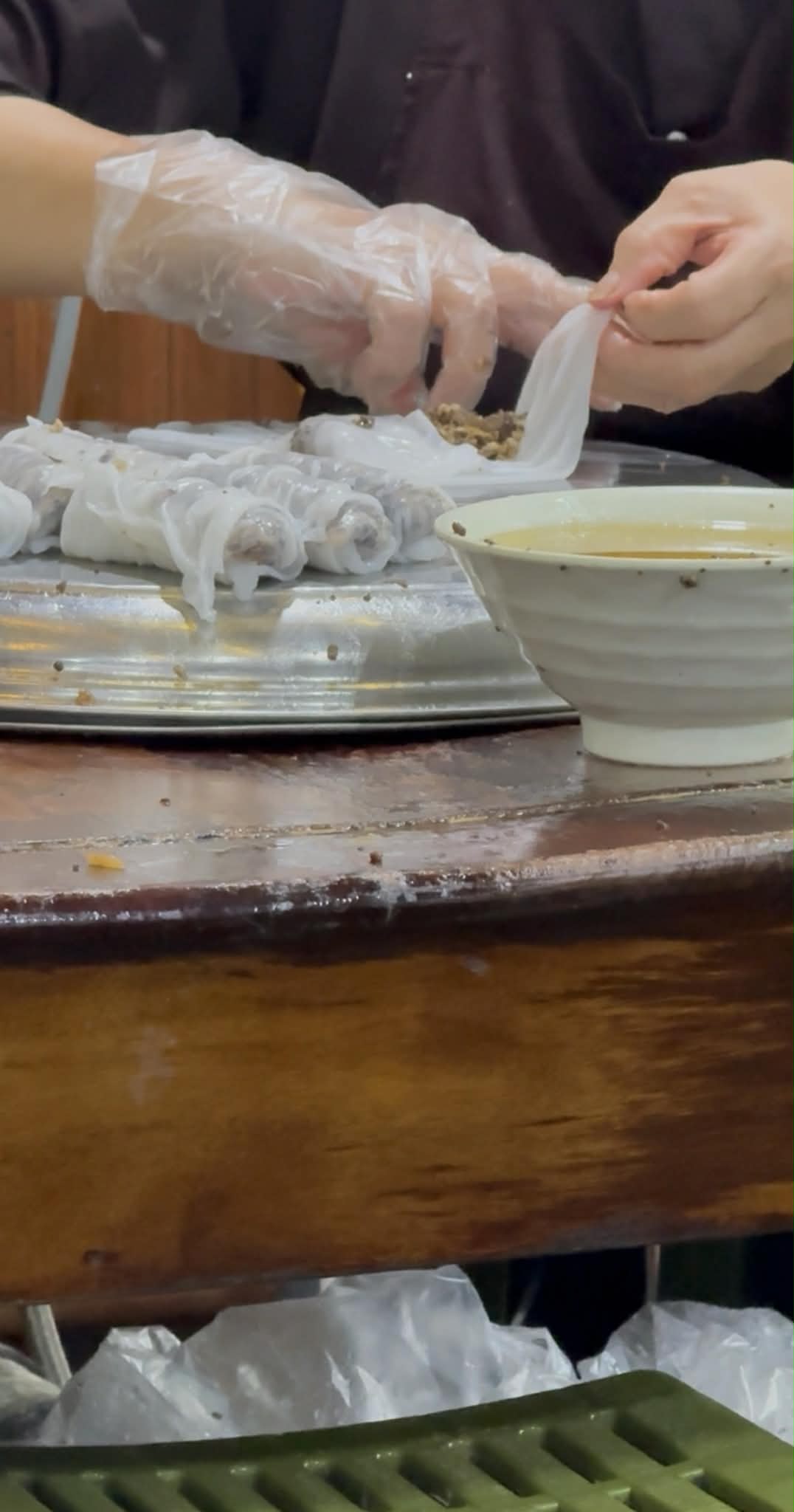 ハノイのバインクオンの作業台で、薄い米皮に餡を包み込んでいる手作業の様子。蒸皮から一皿へ至る中間の工程が見える。