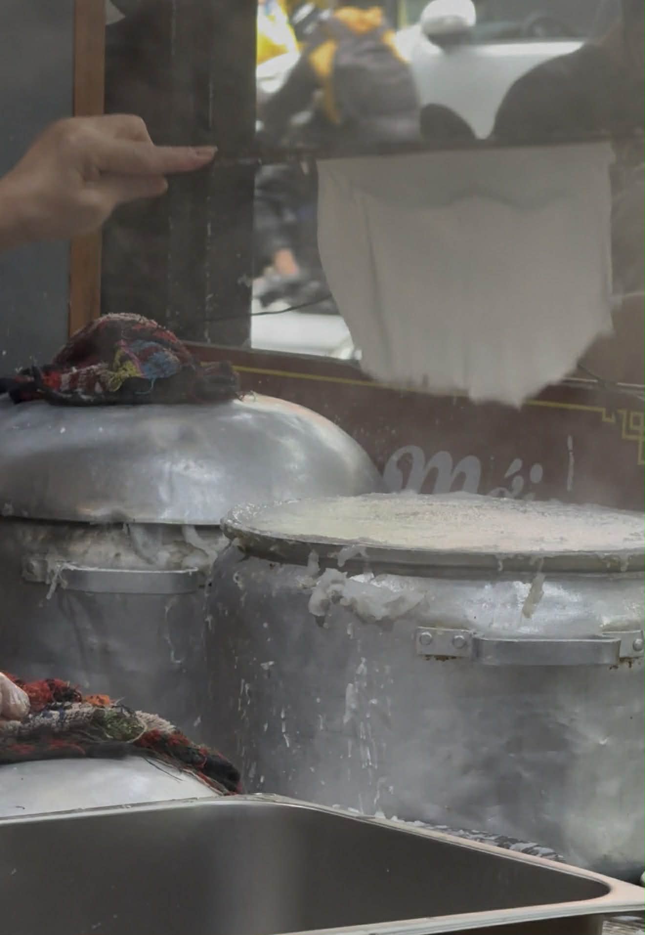 ハノイのバインクオン作りで、蒸布の上で薄く蒸し上がった米皮を竹の道具で持ち上げている場面。蒸皮技術の核心が見える一瞬。