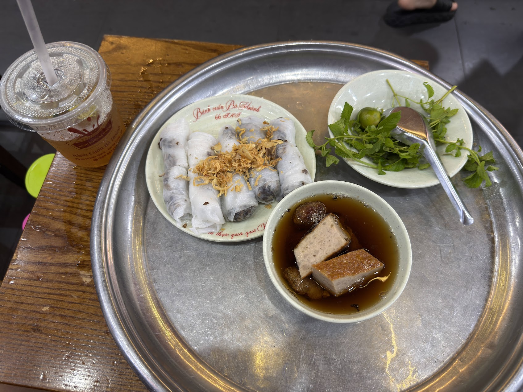 ハノイの街角で供されるバインクオン。澄んだスープ、香草、飲み物が添えられ、米食と湯食が日常の食卓の中で結びついている様子が見える。