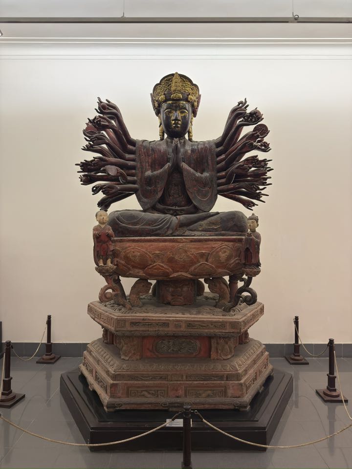 Front view of the thousand-armed Avalokiteśvara in the Vietnam National Museum of Fine Arts, showing radiating arms, a heavy lotus pedestal, and the grounded visual presence of a southern sacred form.