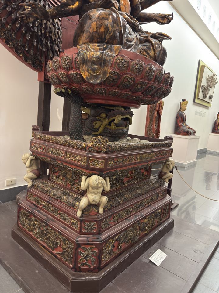 Side view of the thousand-armed Avalokiteśvara in the Hanoi museum, clearly showing the Nāga-supported base beneath the lotus pedestal and the local translation of Buddhist compassion into a Southeast Asian sacred context.