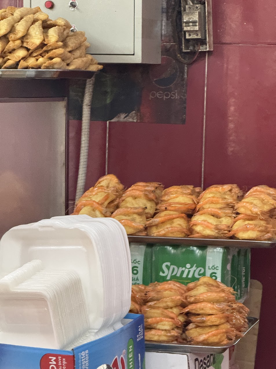 ハノイの街角の朝食屋台に並ぶ海老入り揚げ物。金色に揚がった表面から、朝の熱気と油の香りがまっすぐ伝わってくる。