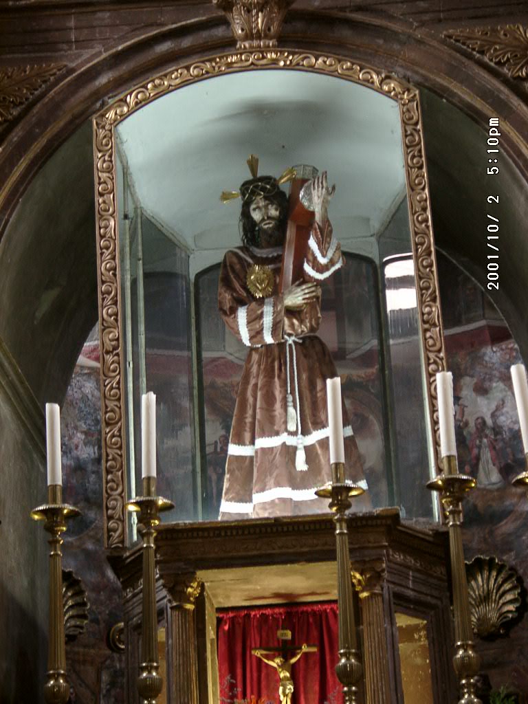 A suffering Jesus statue in Mexico wearing a brown robe, with strong bodily emphasis on wounds and Passion devotion, expressing the distinctly Latin American nearness of sacred suffering to human life.
