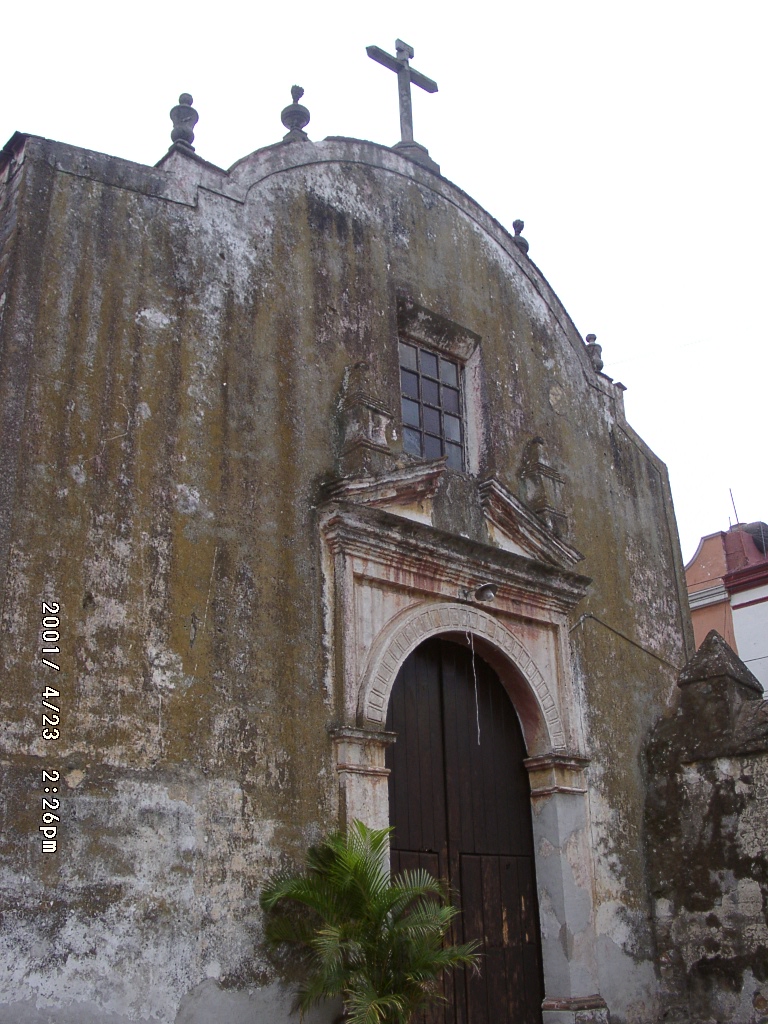 A weathered chapel facade in Mexico with peeling surfaces and visible marks of time, showing how faith settles into local architecture through age and use.