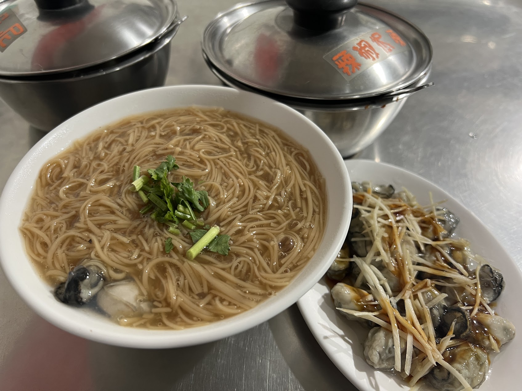蚵仔麵線の横に、薑絲を添えた新鮮な蚵仔の皿が置かれ、麵線と海味の取り合わせが見える