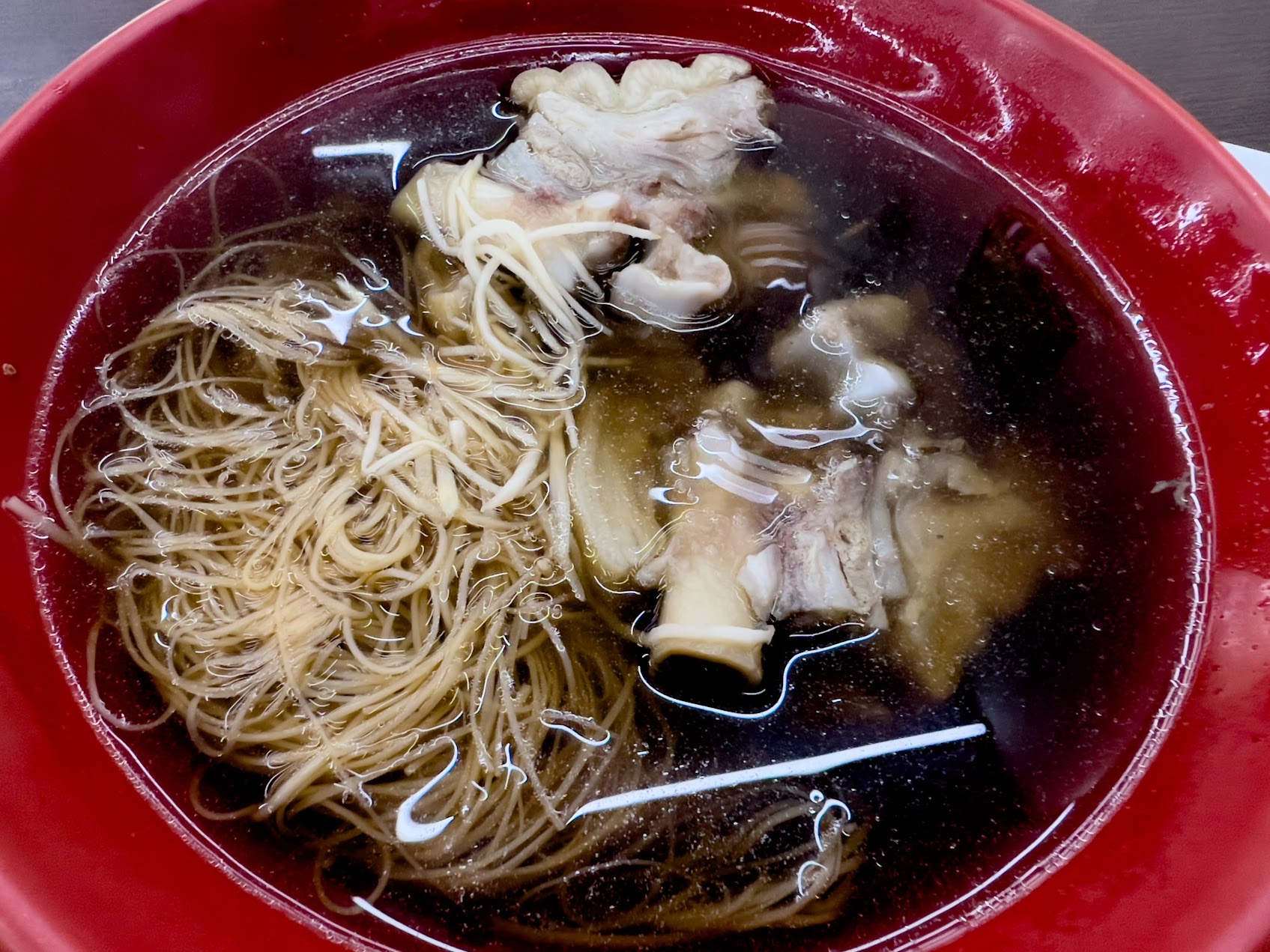 赤い器に盛られた豬腳麵線。澄んだ湯の中に細い麵線と骨付きの豚足が入っている