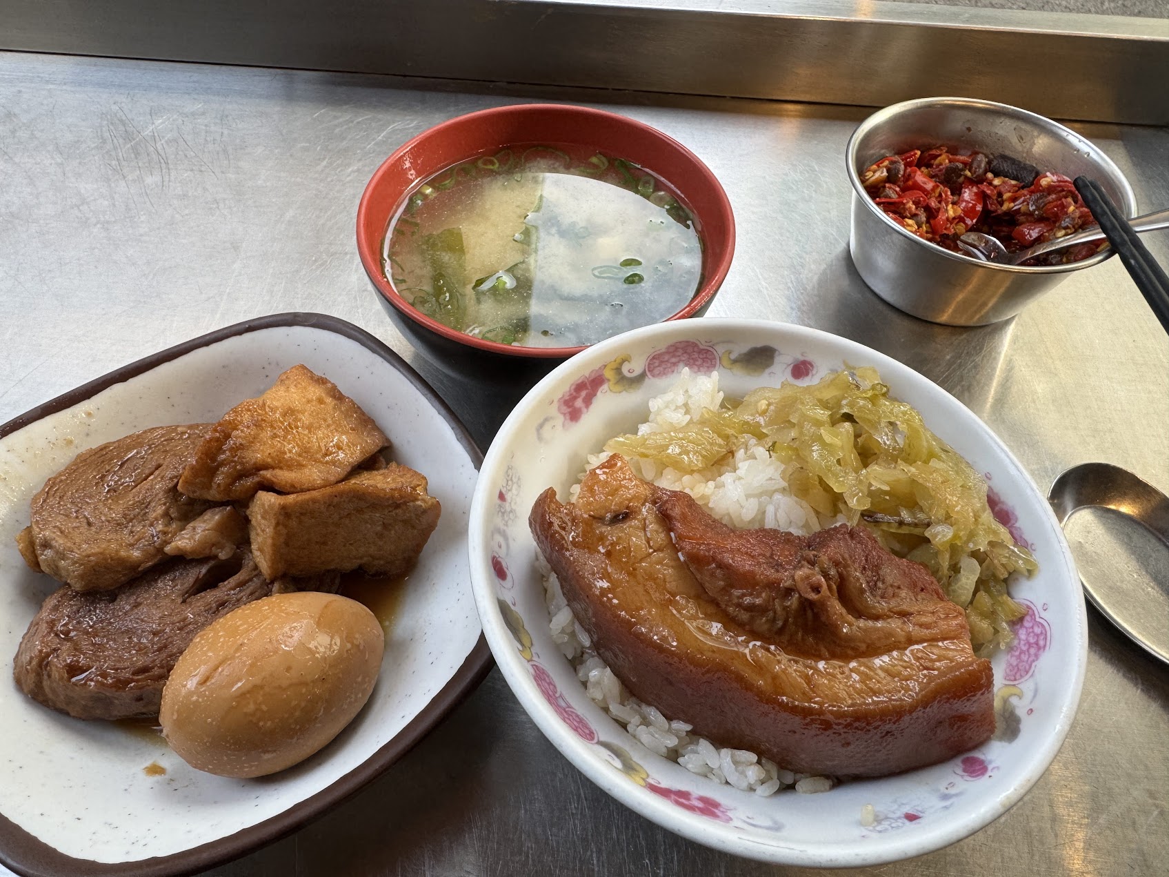 金属のテーブルの上に、爌肉飯、味噌湯、煮卵、豆腐、薬味の皿が並び、台湾の食堂らしい一食の全体像を示している。