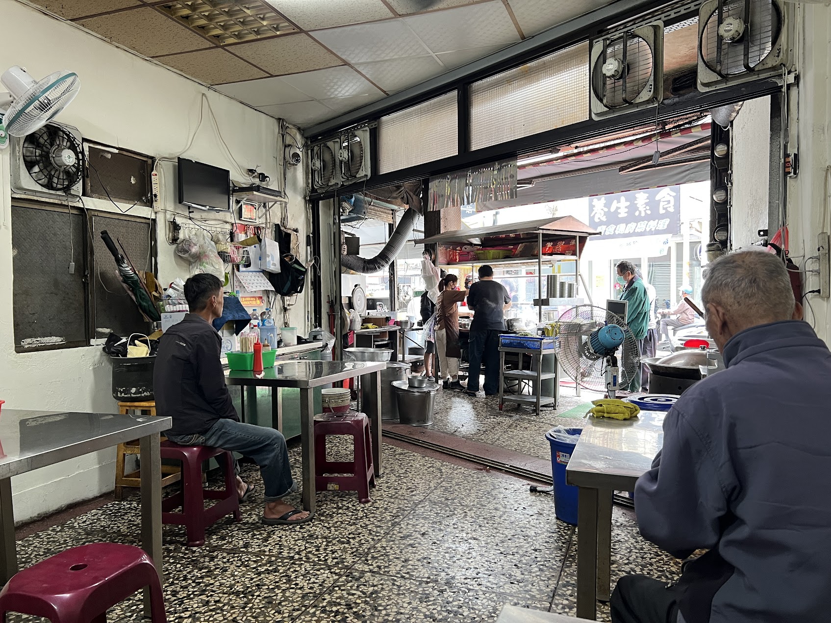 金属の机と椅子、古い扇風機、通りに向かって開かれた店先を持つ、台湾の昔ながらの食堂の内部。