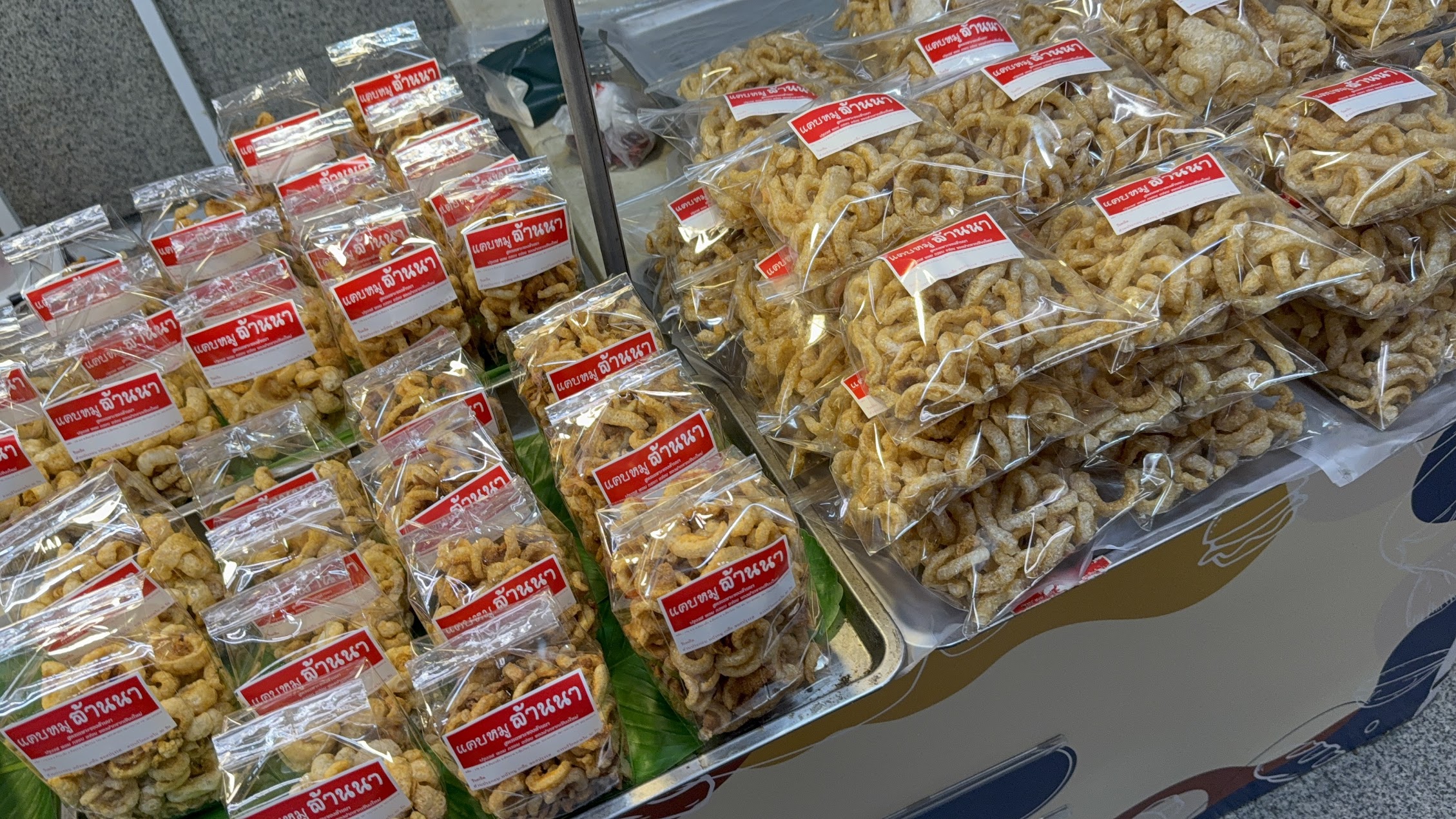 タイの市場に並ぶ袋詰めの豚皮揚げ。揚げた皮類が日常の小売と携帯型零食のシステムに入っていることを示している。