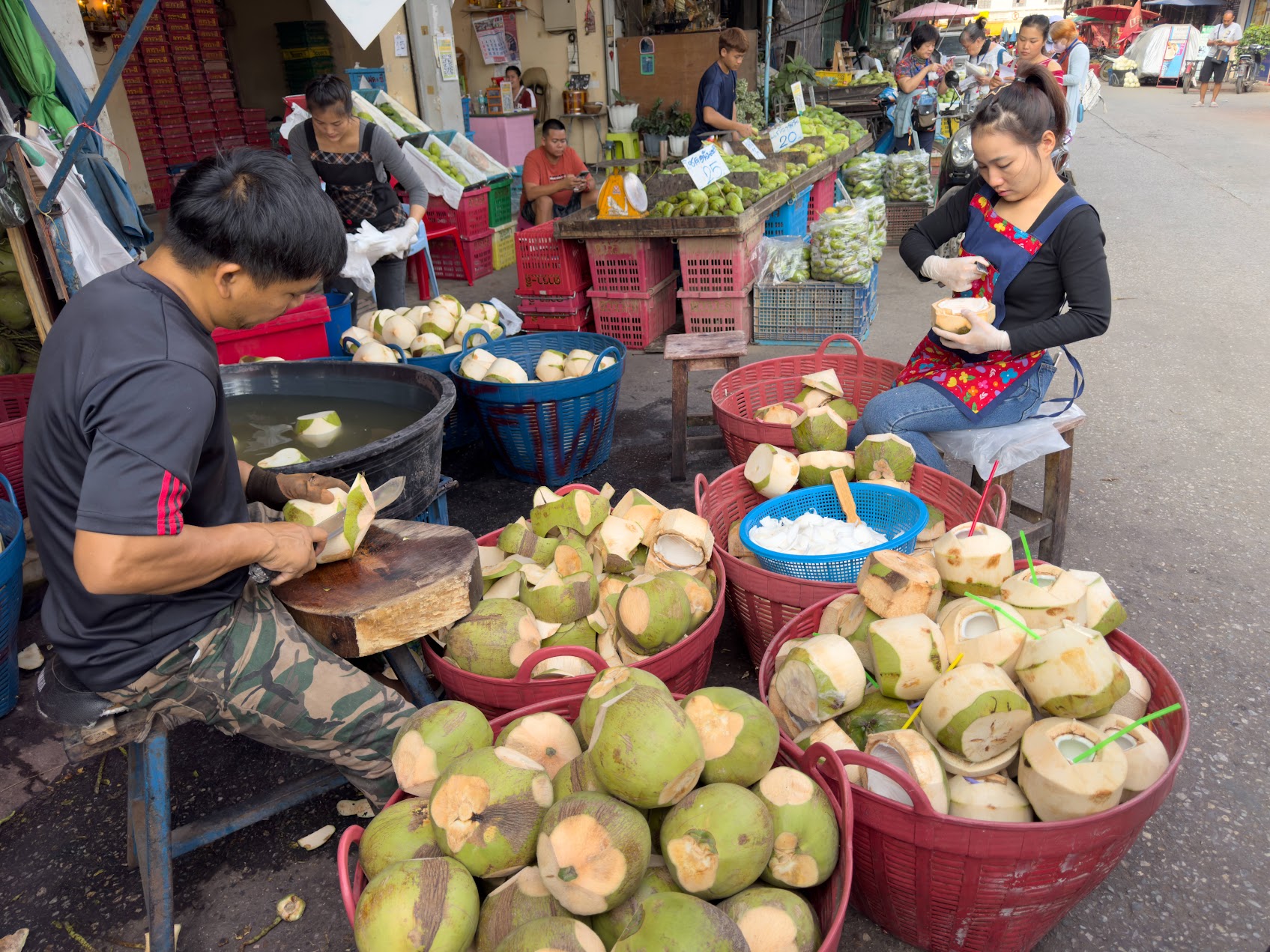 タイの市場で作業者がココナッツを処理している様子。収穫後処理、即食化、付加価値化された果物サプライチェーンの現場を示している。