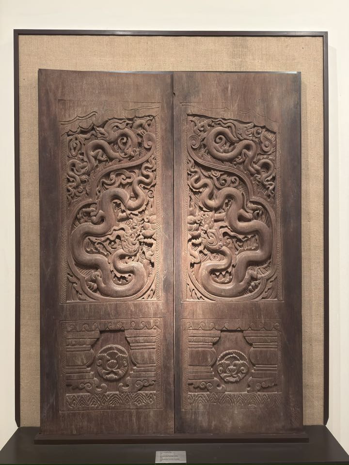 Wood-carved temple door panel in Vietnam showing serpent or Nāga imagery, indicating that the Nāga motif extends beyond pedestal imagery into broader architectural and decorative language.