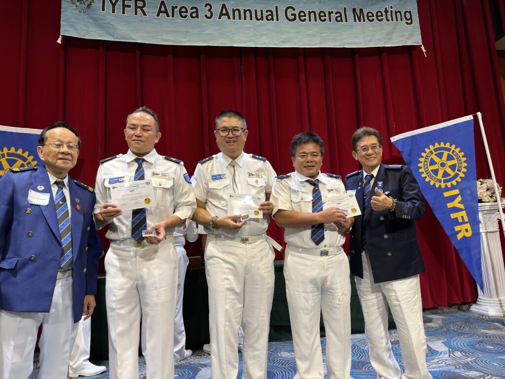 IYFR Area 3 年度會員大會表彰場次，五位與會者於會場橫幅前合影，三人手持獎狀，最左為 Area 3 區總監 Edmond Aguilar，右側懸掛 IYFR 隊旗