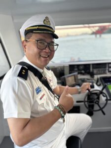 Nelson Chou 穿船長制服站在遊艇駕駛舵位